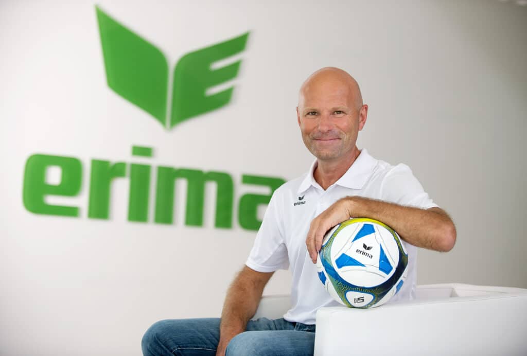 Homme avec un ballon de football devant le logo Erima